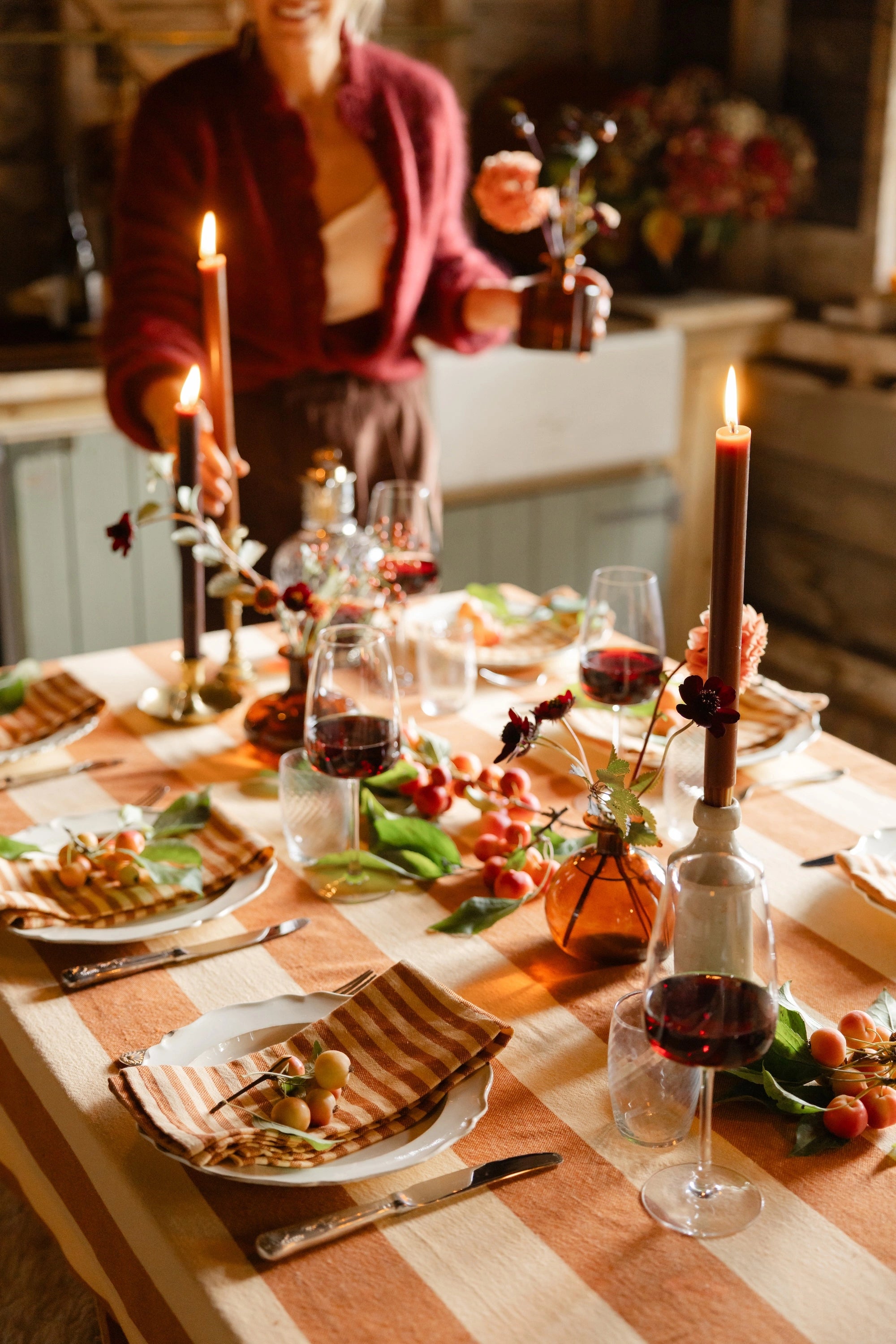 Dining table set for a meal with wine glasses, candles, and food, person in the background.