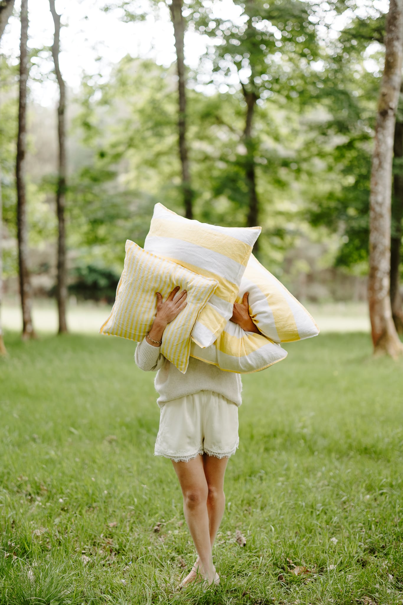 Person holding multiple pillows in a grassy outdoor setting