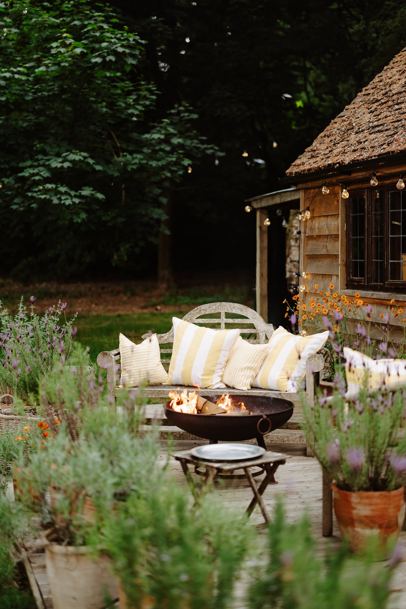 Outdoor patio with a fire pit, striped cushions, and a wooden cabin in the background.