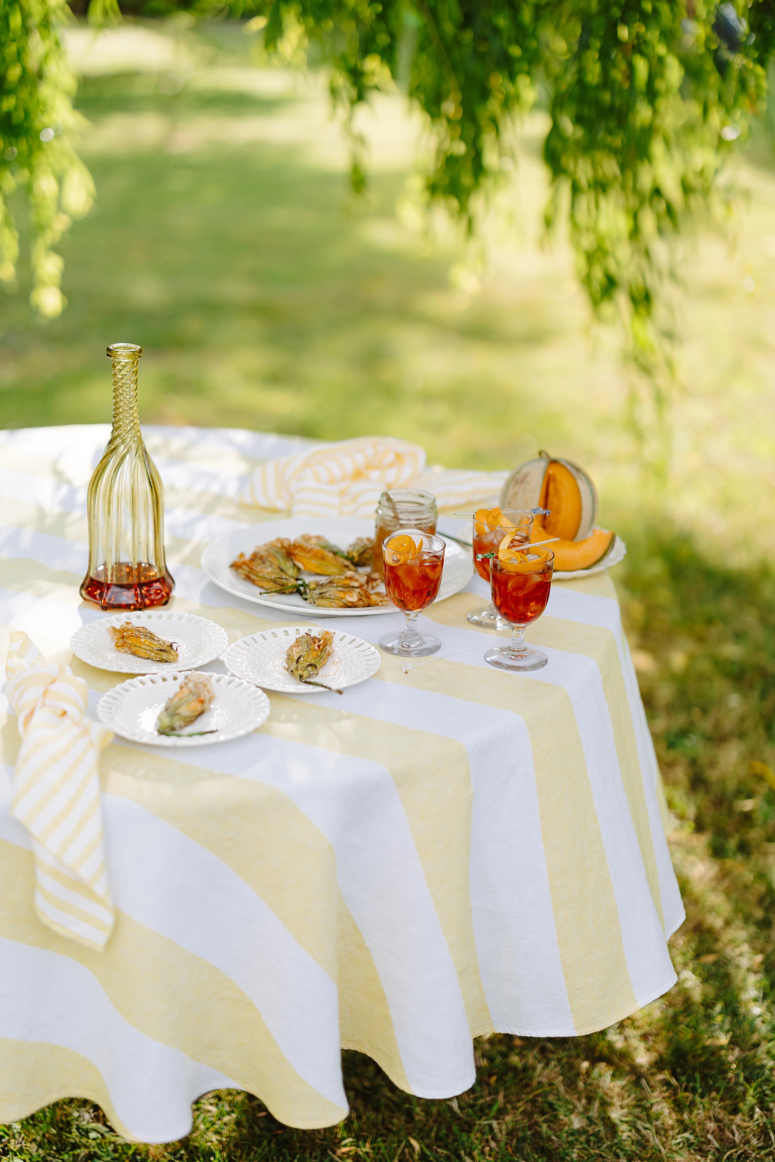 Outdoor table setting with a striped tablecloth, food, and drinks on a grassy background