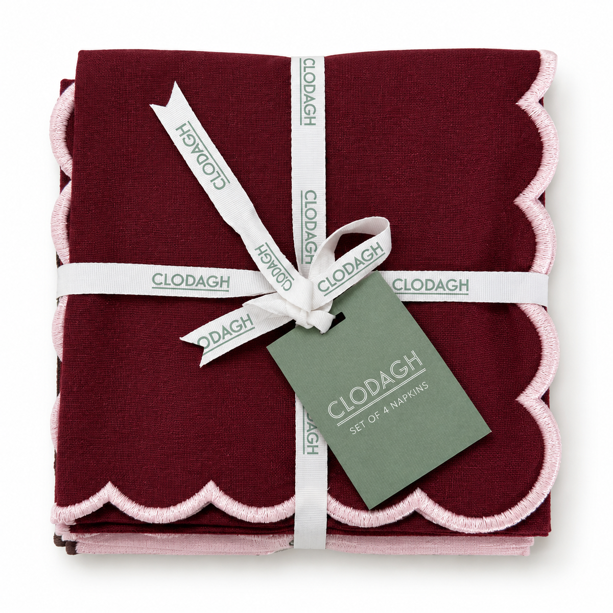 A folded set of four Clodagh napkins in deep burgundy with light pink scalloped edges, wrapped in a white ribbon and a green paper tag.