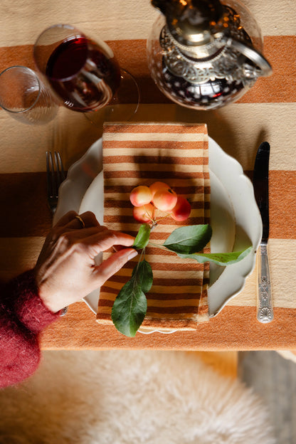 Person arranging flowers on a wooden cutting board over a plate with a glass of red wine and teapot in the background.