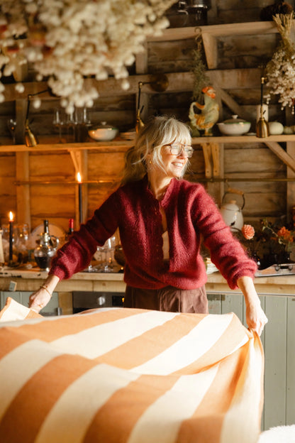 Woman in a cozy kitchen setting with wooden walls and decorative items.