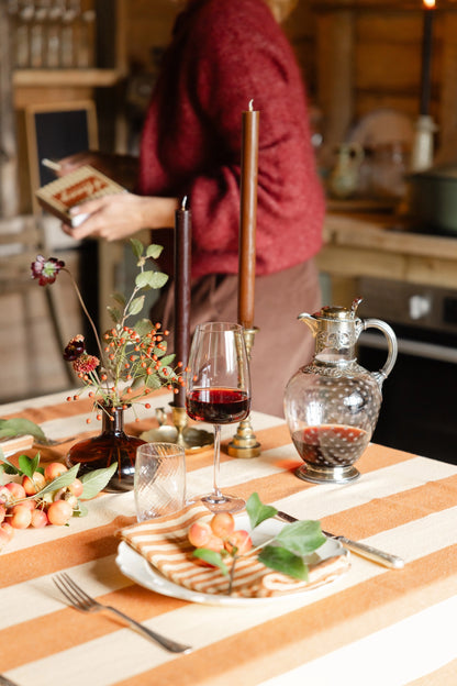 Person in a kitchen setting with a table set for a meal, featuring a glass of red wine.