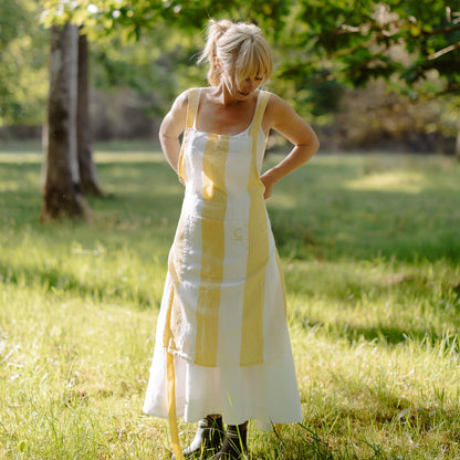 Woman in a yellow and white dress standing in a grassy field with trees in the background