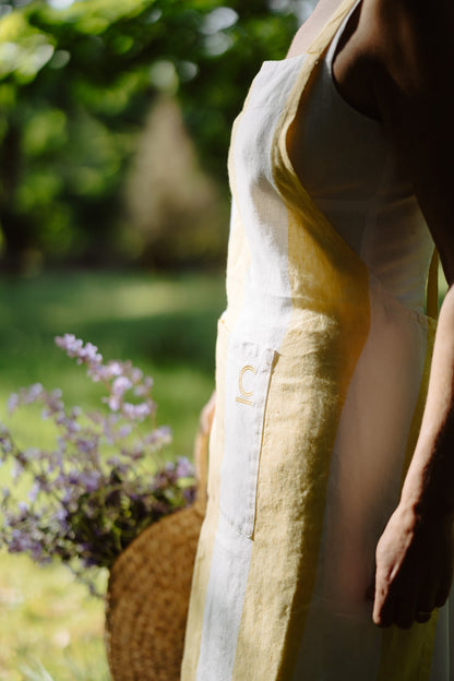 Person wearing a white tank top and yellow apron in a garden setting with blurred background