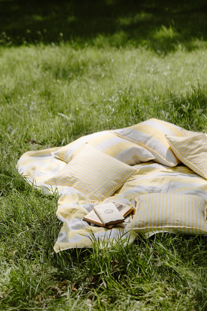 Yellow and white striped blanket with pillows and a book on grass