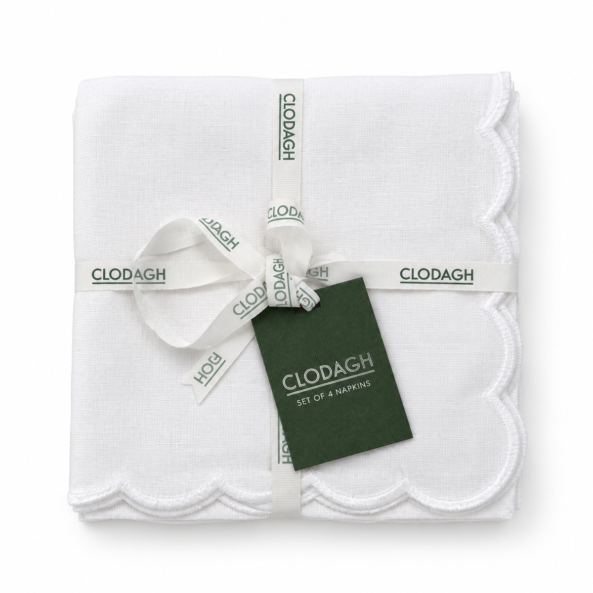 A folded set of four white cotton napkins with scalloped edges, wrapped in a white ribbon printed with the CLODAGH brand name and a dark green product tag.
