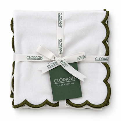 A set of four folded white napkins with olive green scalloped edges, wrapped in a white ribbon printed with the CLODAGH brand name and tied with a dark green brand tag.