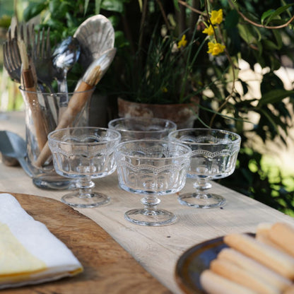 Clear glass trifle bowl dessert serveware on a wooden table with outdoor plants in the background